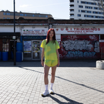 Runner wearing a bright yellow running tee and race shorts standing on a street with a store and graffiti in the background